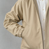 A detail focused photography of a Beige water-repellent made in japan jacket worn over a finely designed white oxford shirt on a gray hand-painted background.
Artisanal approach, Designed in Switzerland, Made in Japan.