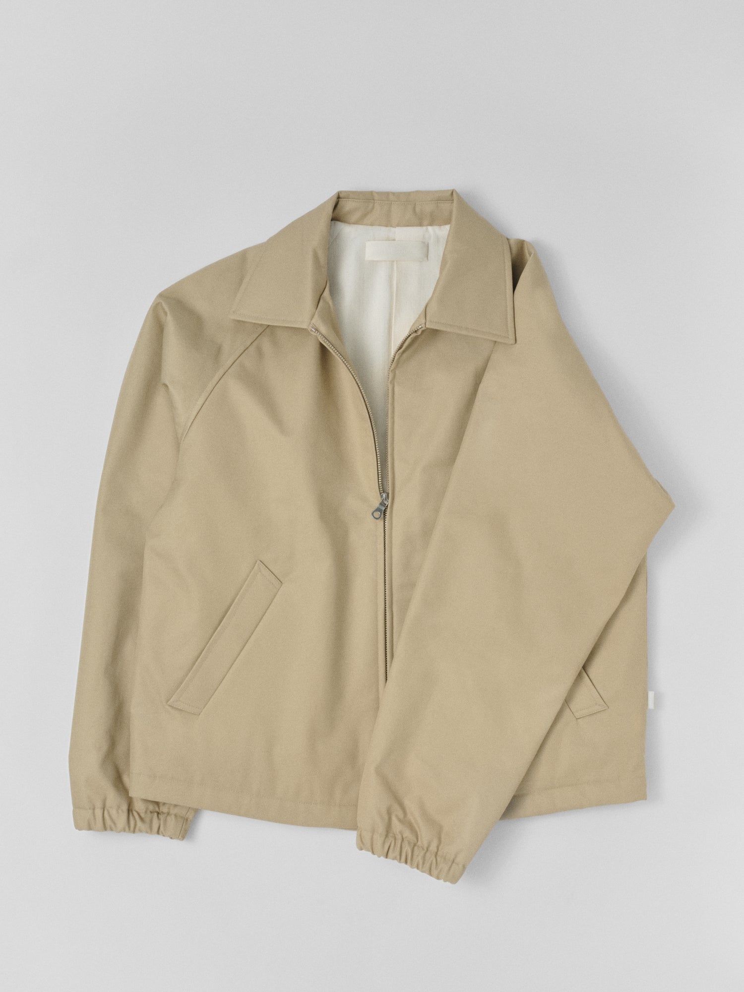 Top-shot photograph of a made in japan Beige water-repellet jacket with a YKK zipper on a light gray background.
Artisanal approach, Designed in Switzerland , Made in Japan